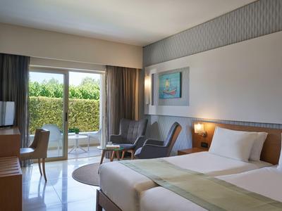 Camera d'albergo luminosa con letto matrimoniale, poltrone, scrivania e accesso al giardino.