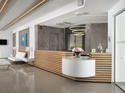 Area reception moderna con banco in legno, sedie bianche e composizione floreale in hotel.