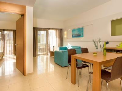 Camera d'hotel moderna con angolo pranzo, zona salotto, balcone, pavimento luminoso e illuminazione calda.