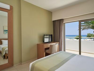 Camera d'hotel con letto matrimoniale, scrivania, TV e terrazza con vista mare.