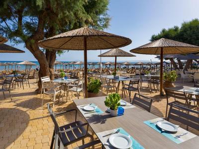 Venkovní restaurace s stolem, židlemi a slunečníky na pláži s výhledem na moře.