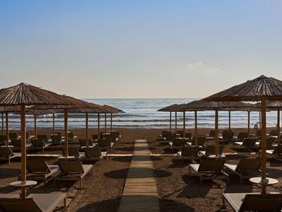 Spiaggia con lettini e ombrelloni di paglia vicino a un mare calmo sotto un cielo limpido.