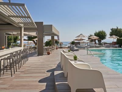 Area piscina moderna di un hotel con lettini, sgabelli e vista sul mare.