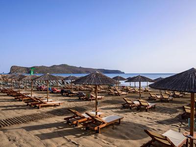 Fila di lettini e ombrelloni di paglia su una spiaggia sabbiosa tranquilla sotto un cielo limpido.