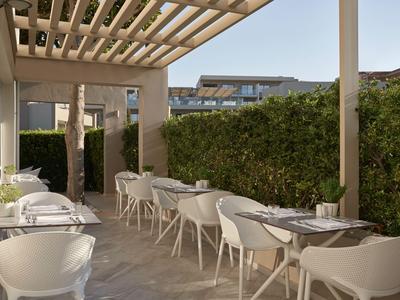 Moderna terrazza esterna con mobili bianchi e tetto in legno, circondata da siepi verdi.