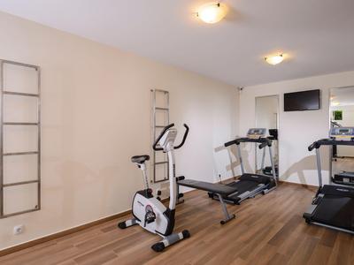 Salle de sport moderne avec tapis roulants, vélo d'intérieur et sol en bois dans une pièce lumineuse.