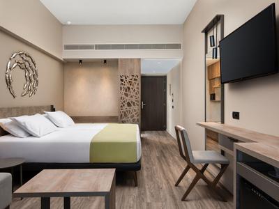 Moderní hotelový pokoj s manželskou postelí, nástěnným uměním a televizí vedle stolu a židle.