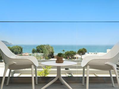 Zwei weiße Stühle auf einer Terrasse mit Blick auf das Meer und blauem Himmel.