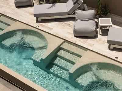 Espace piscine moderne avec deux sections de bain à remous rondes et chaises longues.