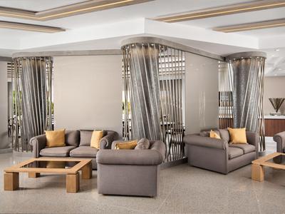 Salon moderne d'hôtel avec canapés gris, tables en bois et rideaux gris.