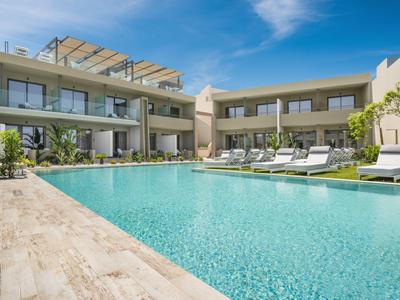 Piscine d'hôtel moderne avec chaises longues et vue sur deux bâtiments à plusieurs étages sous un ciel bleu.