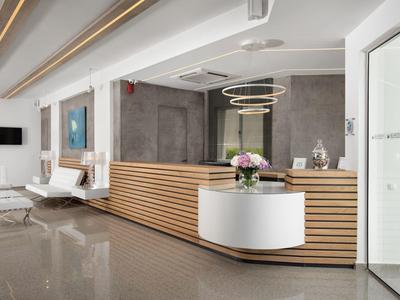 Moderní hotelová nebo kancelářská recepce s dřevěným pultem, bílým stolem a květinovou výzdobou.