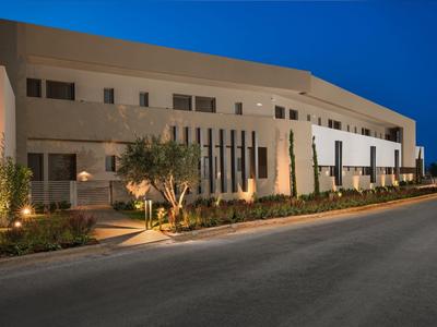 Moderní osvětlená hotelová budova za soumraku s upravenou zelení.