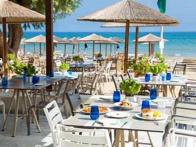 Terrasse extérieure d'un restaurant de plage avec des tables blanches, verres bleus et parasols au bord de la mer.
