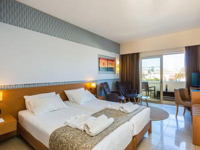 Světle zařízený hotelový pokoj se dvěma postelemi, balkonem a posezením.