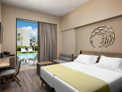 Moderní hotelový pokoj s manželskou postelí, stolem, pohovkou a výhledem na bazén.