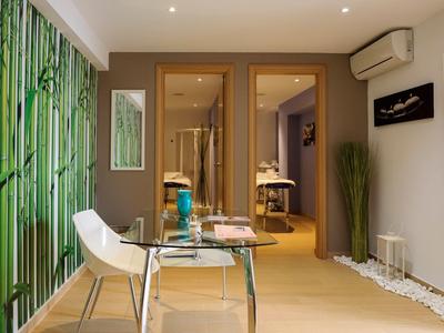 Moderní wellness pokoj s masážním stolem, skleněným stolkem a zelenou bambusovou výzdobou.