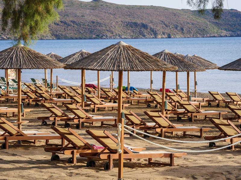 Prázdná dřevěná lehátka se slámovými slunečníky na písčité pláži u klidného moře.