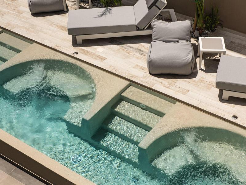 Moderní bazén se dvěma kulatými vířivkami a lehátky na světlé terase.