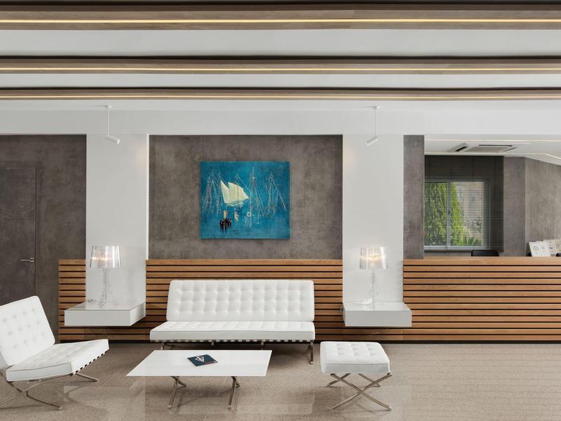 Moderní hotelová lobby s bílým posezením, dřevěnými detaily a abstraktním modrým obrazem na zdi.