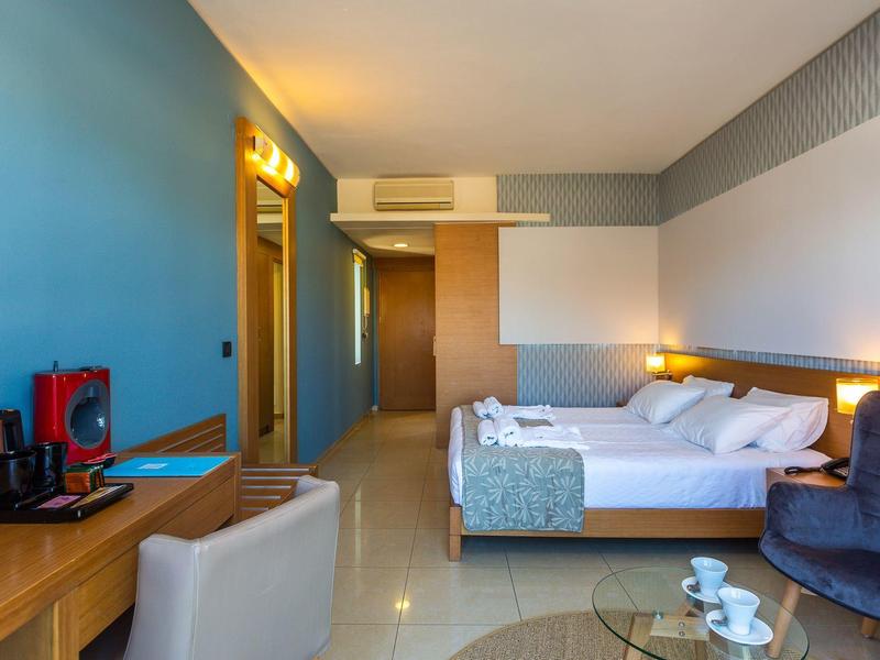 Moderní hotelový pokoj s manželskou postelí, psacím stolem, kávovarem a pohodlnými křesly.