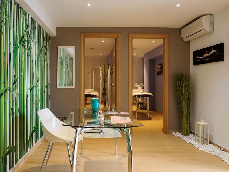 Moderní wellness pokoj s masážním stolem, skleněným stolkem a zelenou bambusovou výzdobou.