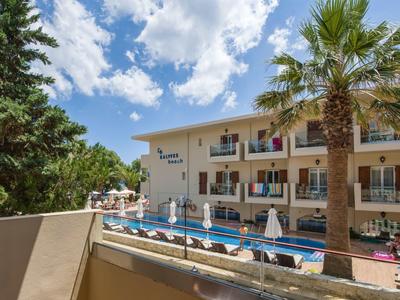 Hôtel avec piscine, parasols et palmiers sous un ciel bleu avec des nuages.