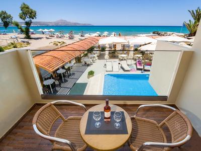 Vue depuis un balcon avec table, deux chaises et bouteille de vin sur piscine, plage et mer