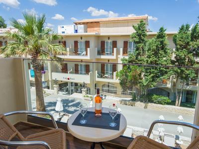 Vue du balcon sur un hôtel moderne avec tables, chaises et arbres par temps ensoleillé.