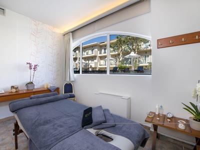 Salle de massage confortable avec table de massage bleue, tables en bois et fenêtre donnant sur un hôtel.