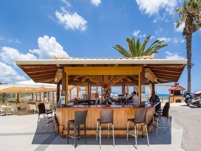 Bar de plage avec des tabourets sous un toit en bois et ciel ensoleillé.
