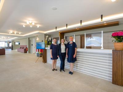 Drei Hotelangestellte stehen am Empfangsbereich mit moderner Rezeption und heller Innenausstattung.