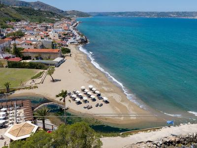 Ville côtière avec plage de sable, parasols, mer turquoise et maisons groupées devant des montagnes.