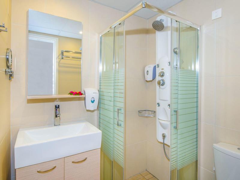 Salle de bain moderne avec douche d'angle, lavabo et miroir aux couleurs neutres.