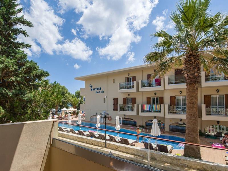 Hôtel avec piscine, parasols et palmiers sous un ciel bleu avec des nuages.