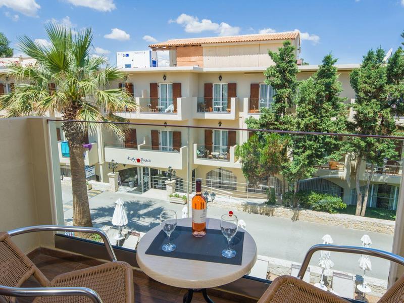 Vue du balcon sur un hôtel moderne avec tables, chaises et arbres par temps ensoleillé.
