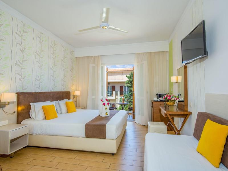 Chambre d'hôtel lumineuse avec lit double, canapé, balcon et décoration moderne.