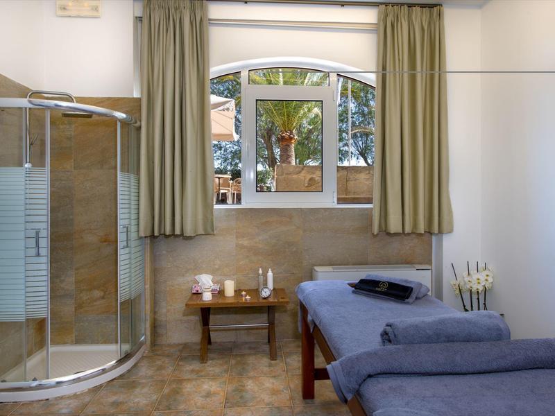 Salle de bien-être lumineuse avec table de massage, cabine de douche et grande fenêtre avec rideaux.