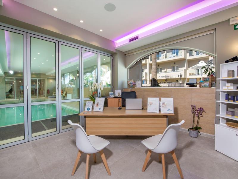 Réception moderne avec des chaises claires, un comptoir en bois et de grandes fenêtres en verre dans un hôtel.