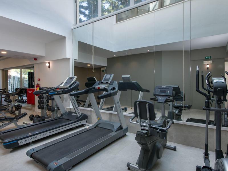Salle de sport moderne avec tapis de course, elliptiques et grands miroirs.