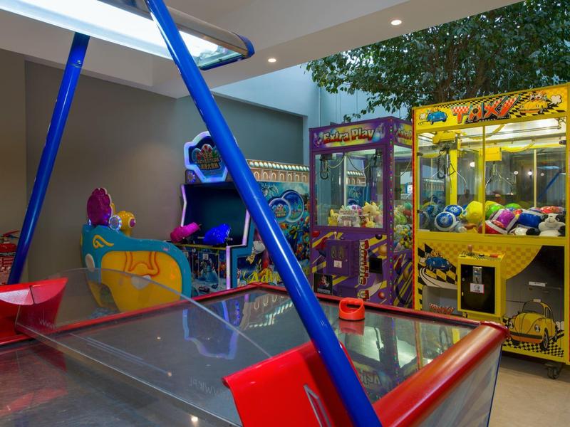 Une salle de jeux avec une table de air hockey, une machine à pince et un flipper.