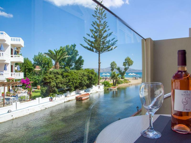 Vue du balcon sur un canal avec des bateaux, une végétation luxuriante et un aperçu de la mer.
