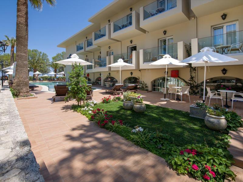 Espace extérieur avec parasols, tables et chaises à côté d'un hôtel sous un ciel dégagé.