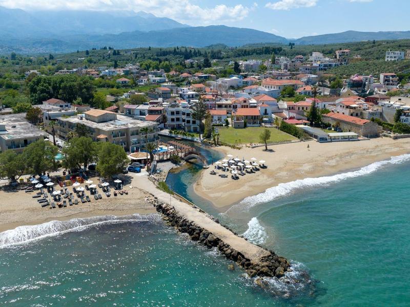 Station balnéaire côtier avec plages de sable, parasols, une jetée et des bâtiments proches sous un ciel bleu.