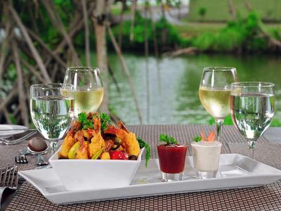 Teller mit buntem Salat, zwei Gläser Weißwein und Wasser stehen auf gedecktem Tisch am Flussufer.