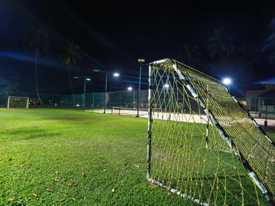 Beleuchteter Fußballplatz bei Nacht mit grünem Rasen und großem Tor im Vordergrund.