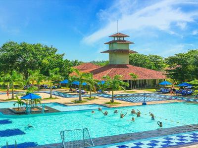 Großer Pool mit blau-weißen Kacheln, Palmen, Sonnenschirmen und einem mehrstöckigen Gebäude im Hintergrund.