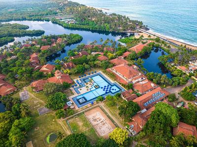 Luftaufnahme eines Resorts mit roten Dächern, Pool, Teichen und Strand am Horizont.