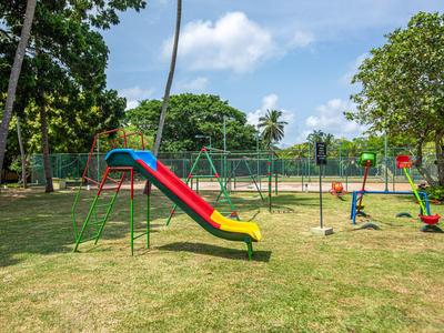 Spielplatz mit roter und gelber Rutsche, Schaukel, grünem Rasen und Bäumen im Hintergrund.