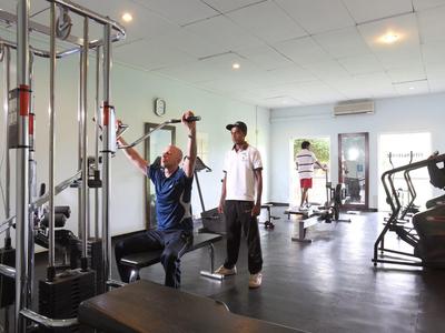 Moderner Fitnessraum mit Trainingsgeräten, zwei Personen beim Krafttraining und hellem Fensterlicht.